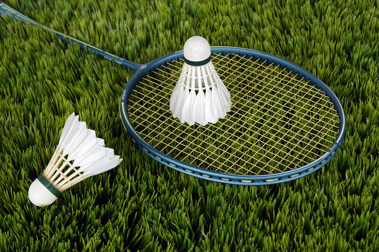 zdjęcie leżącej na trawie rakietki do badmintona wraz z dwola lotkami do gry. zdjęcie z piaxabay.com