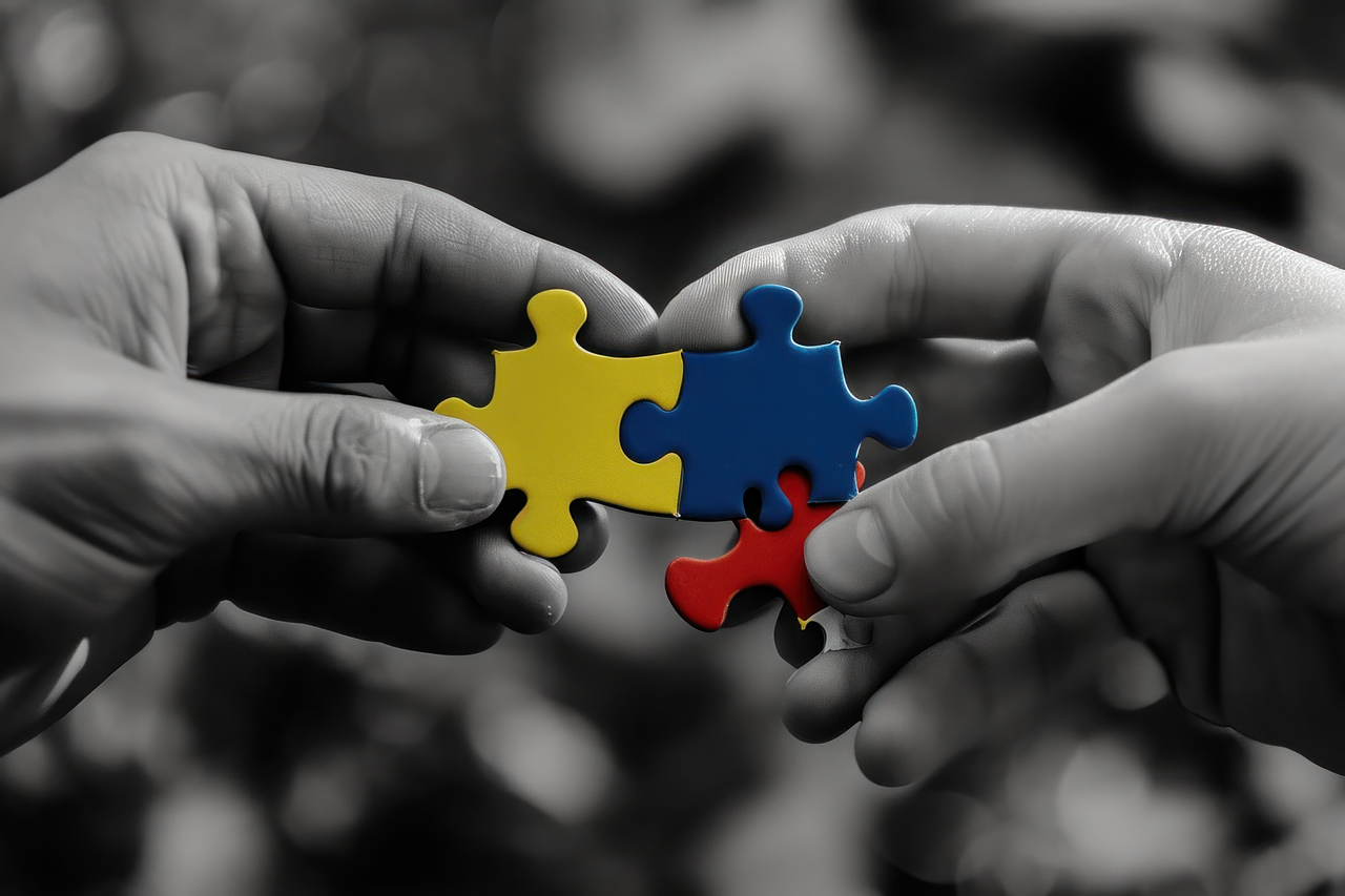 zdjęcie dwóch dłoni trzymające i składające puzzle. Dłonie w odcieniach szarości składają kolorowe puzzle w trzech kolorach: żółty, niebieski, czerwony. zdjęcie ze strony pixabay.com